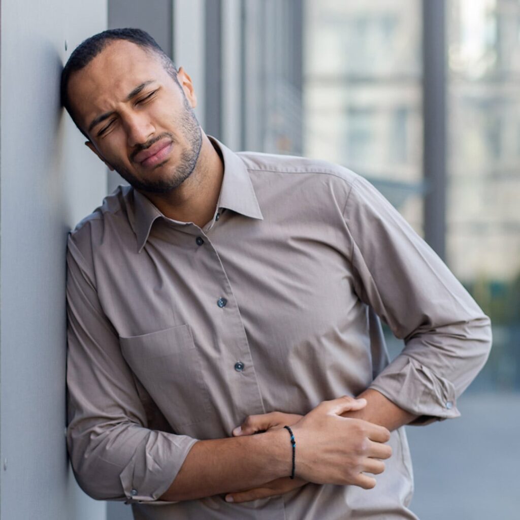 Hombre latino se apoya de una pared, se agarra la barriga y cierra los ojos en dolor