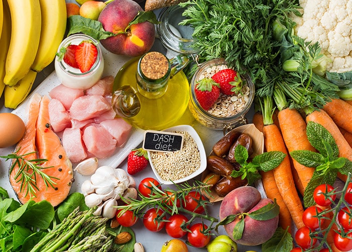 Una mesa de madera repleta de comida saludable, como pechuga de pollo, pescado, vegetales y frutas